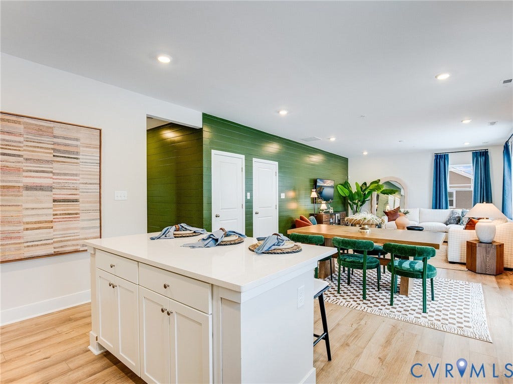 3724 Larimar Lane, Everstone, Richmond, VA 23223 Open-concept kitchen and living area featuring a white cabinetry island with waterfall countertop, recessed lighting throughout, wide-plank wood-finish flooring, and a vibrant green accent wall with built-in shelving and potted plants