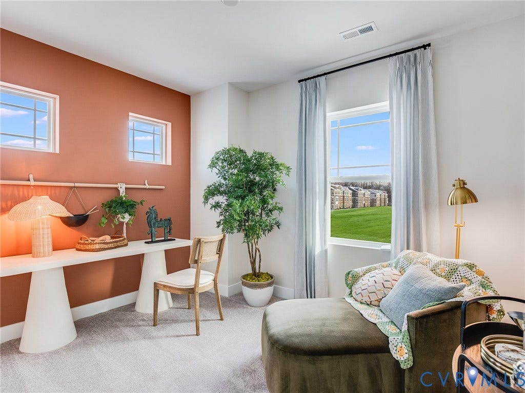 3712 Larimar Lane, Everstone, Richmond, VA 23222 Versatile bedroom suite featuring a vibrant coral accent wall, dedicated workspace with built-in desk and natural light, abundant windows with operable glass doors opening to expansive lawn views, potted greenery, and soft gray carpeting throughout