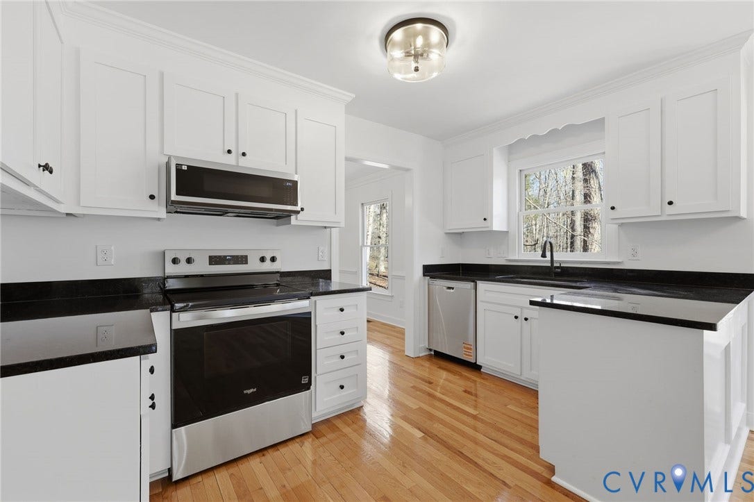 3264 Sherwood Ridge Way, Powhatan, VA 23139 Bright primary bedroom featuring large multi-pane windows with natural light, ceiling fan with integrated lighting, neutral wall finishes, geometric patterned area rug, and wood-finish flooring throughout