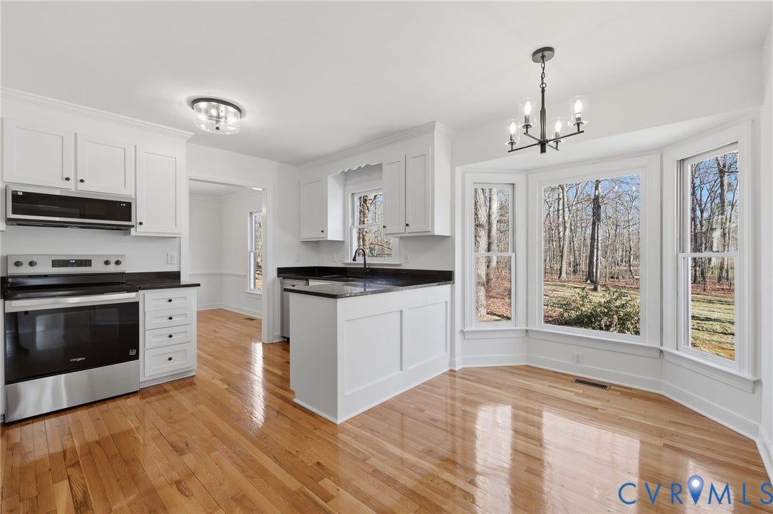 3264 Sherwood Ridge Way, Powhatan, VA 23139 Bright primary bedroom featuring large multi-pane windows with natural light, ceiling fan with integrated lighting, neutral wall finishes, geometric patterned area rug, and wood-finish flooring throughout