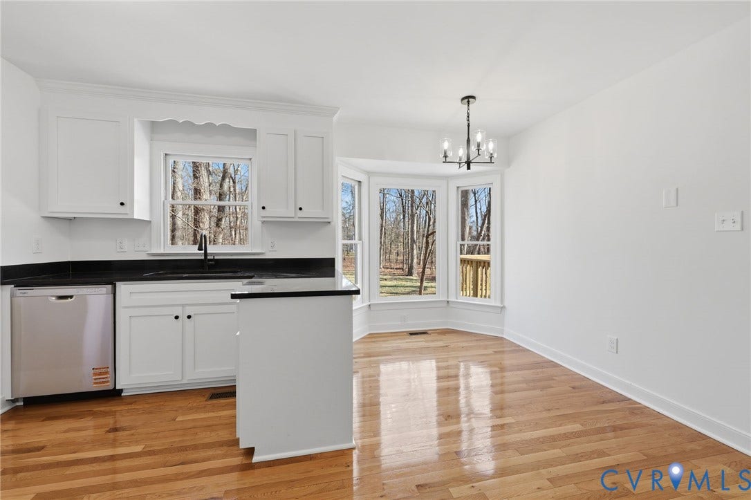 3264 Sherwood Ridge Way, Powhatan, VA 23139 Open-concept kitchen and dining area featuring white cabinetry with hardware accents, black countertops, stainless steel appliances, and hardwood flooring throughout