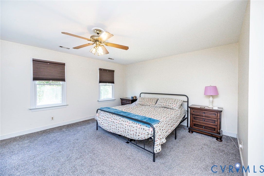 Neutral wall finishes, two windows with blinds, ceiling fan with integrated lighting, and carpeted flooring