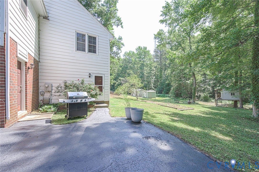 Exterior featuring white siding, brick facade, a paved driveway, and mature trees