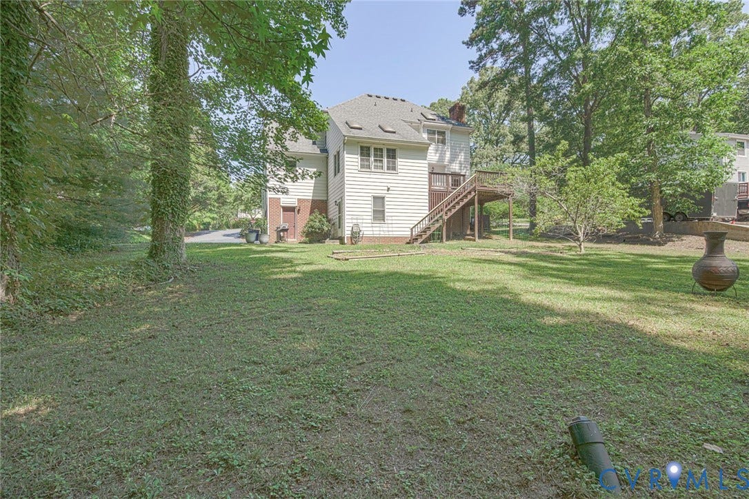 Expansive rear lawn with mature trees and a multi-level deck