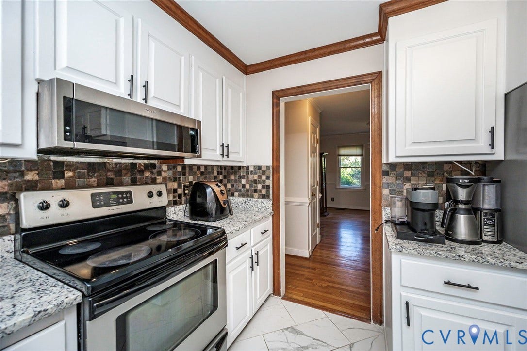 White shaker-style cabinetry with matte black hardware, stainless steel over-the-range microwave, mosaic tile backsplash, and light-toned countertops