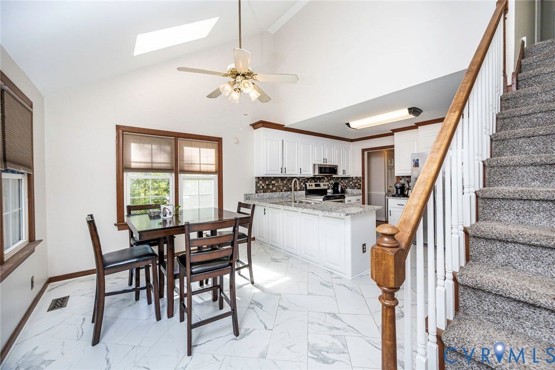 Vaulted ceilings, a kitchen island, white cabinetry, a skylight, and white tile flooring