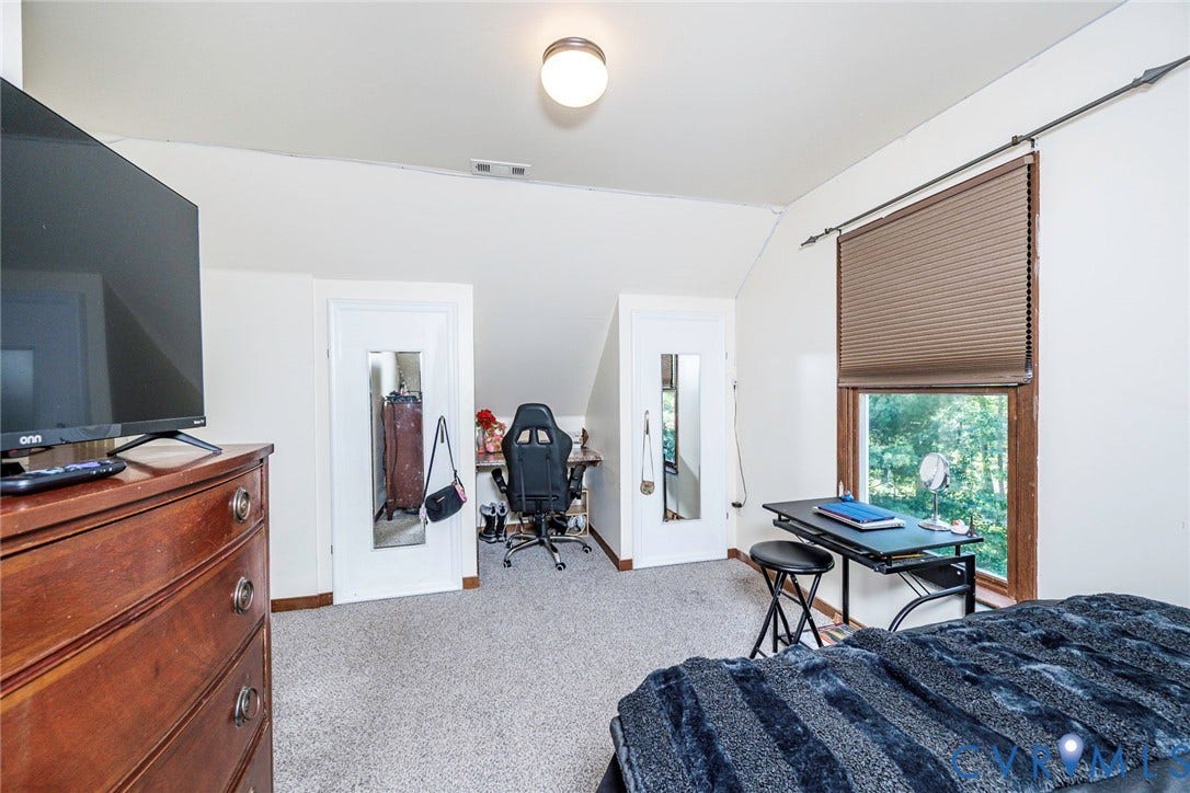 Carpeted flooring with sloped ceilings and a single window with blinds
