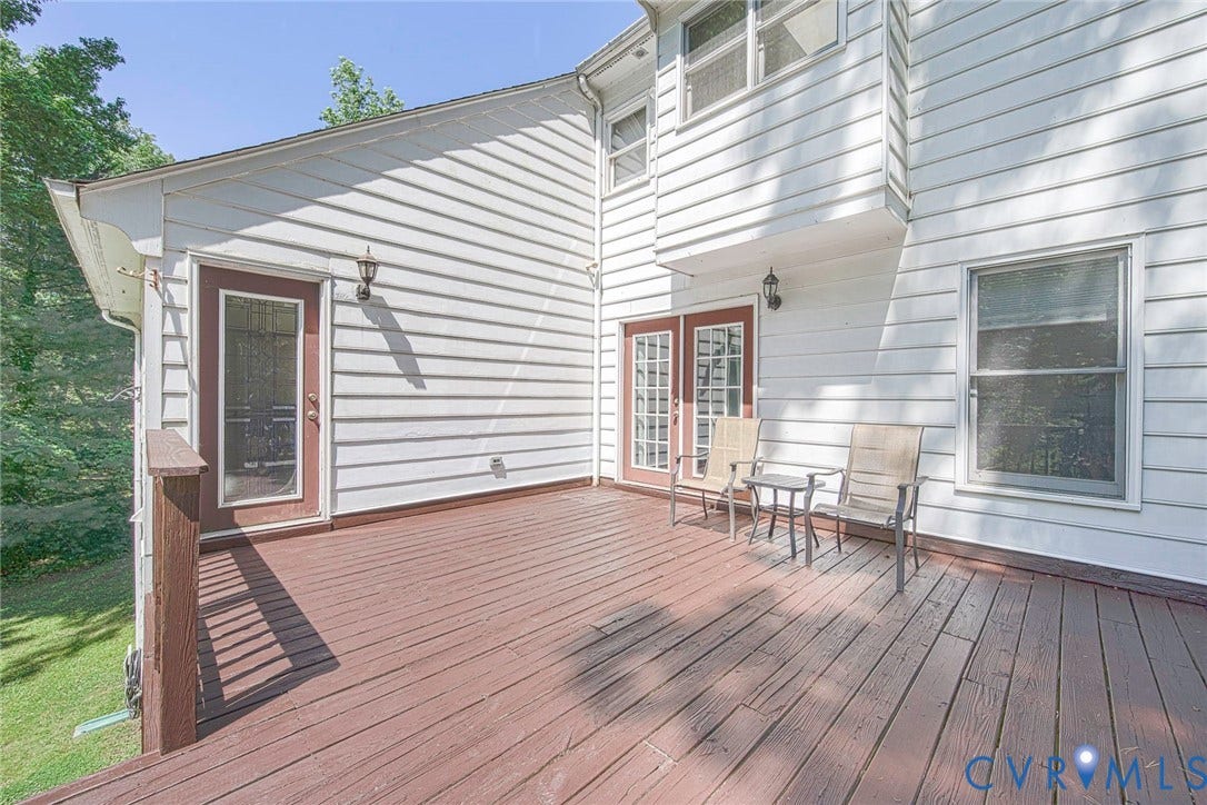 Expansive wood deck with a stained finish, featuring multiple access points including a glass-paneled door and double French doors
