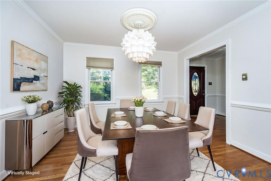 Elegant dining room showcasing hardwood flooring, a round wood dining table, upholstered dining chairs, and a sculptural pendant light fixture
