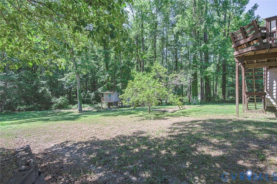 Expansive green lawn with mature trees and a multi-level wood deck