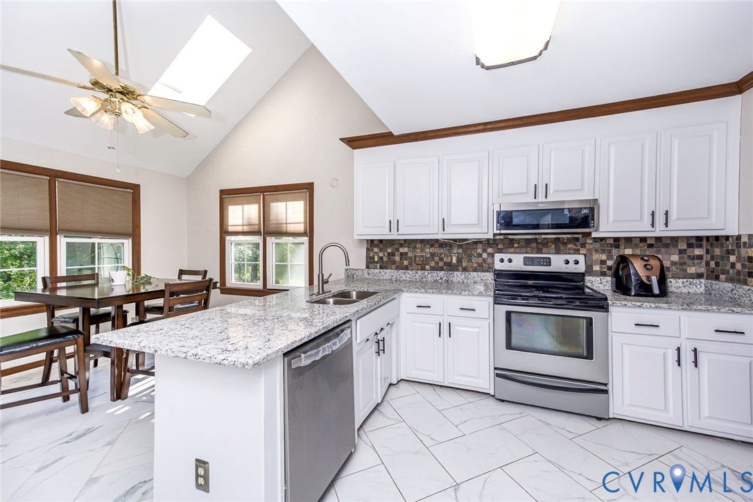 Vaulted ceiling with skylight, white shaker cabinets, stainless steel appliances, granite countertops, and tiled flooring