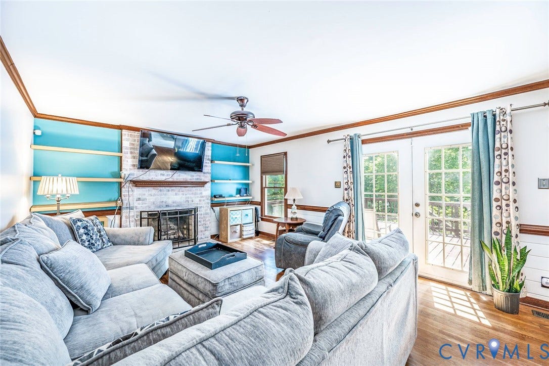 Brick-surround fireplace with hearth, built-in shelving, wood-finish flooring, and a ceiling fan