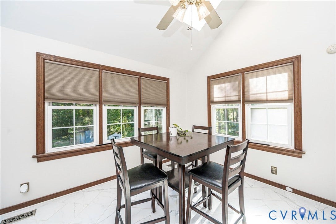 Vaulted ceiling, ceiling fan, multiple windows with natural wood trim, white walls, and white tile flooring