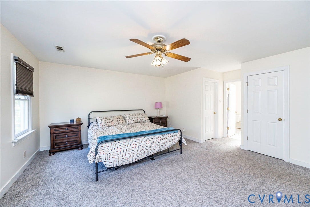 Spacious primary bedroom with neutral carpeting, ceiling fan with integrated lighting, metal bed frame, wood-finish nightstand, and multiple closet doors providing ample storage
