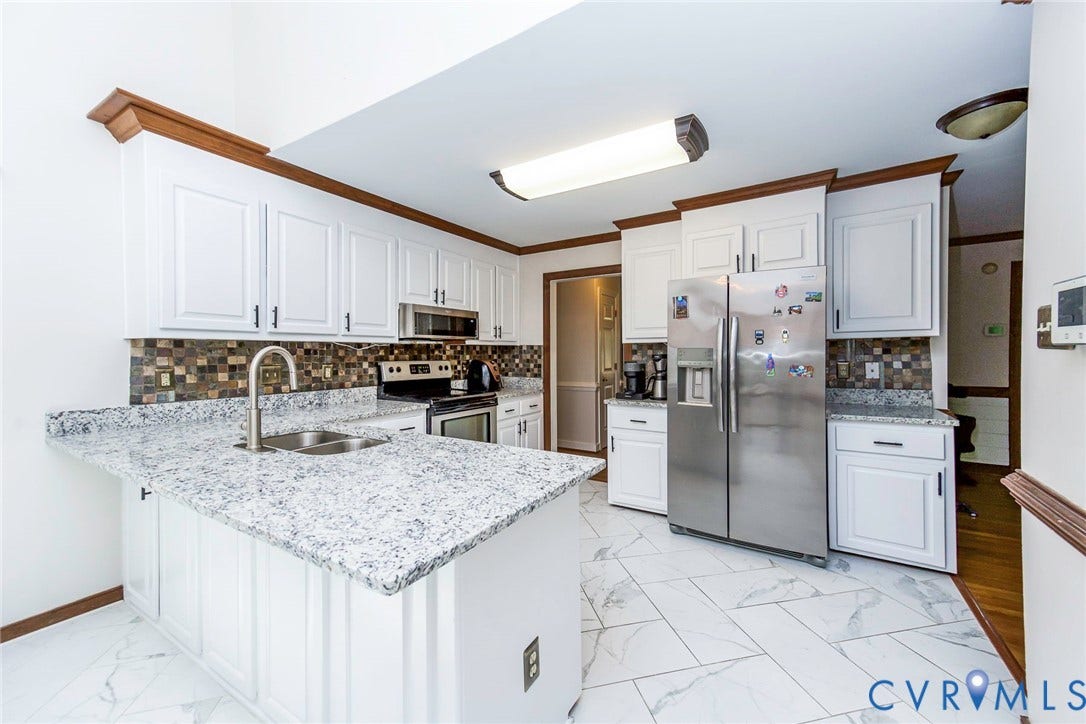 White cabinetry with crown molding, stainless steel appliances, mosaic tile backsplash, light-toned granite countertops, and large format floor tiling