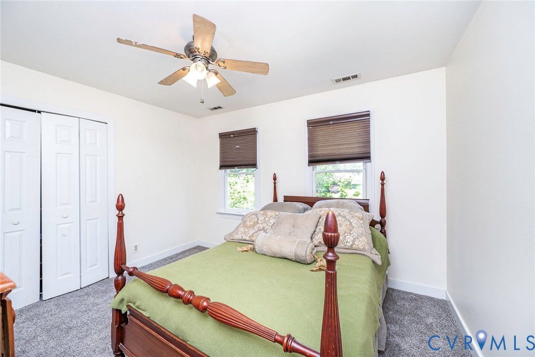 Bright secondary bedroom featuring dual windows with cellular shades, ceiling fan with light fixture, carpeted flooring, and a four-poster bed frame
