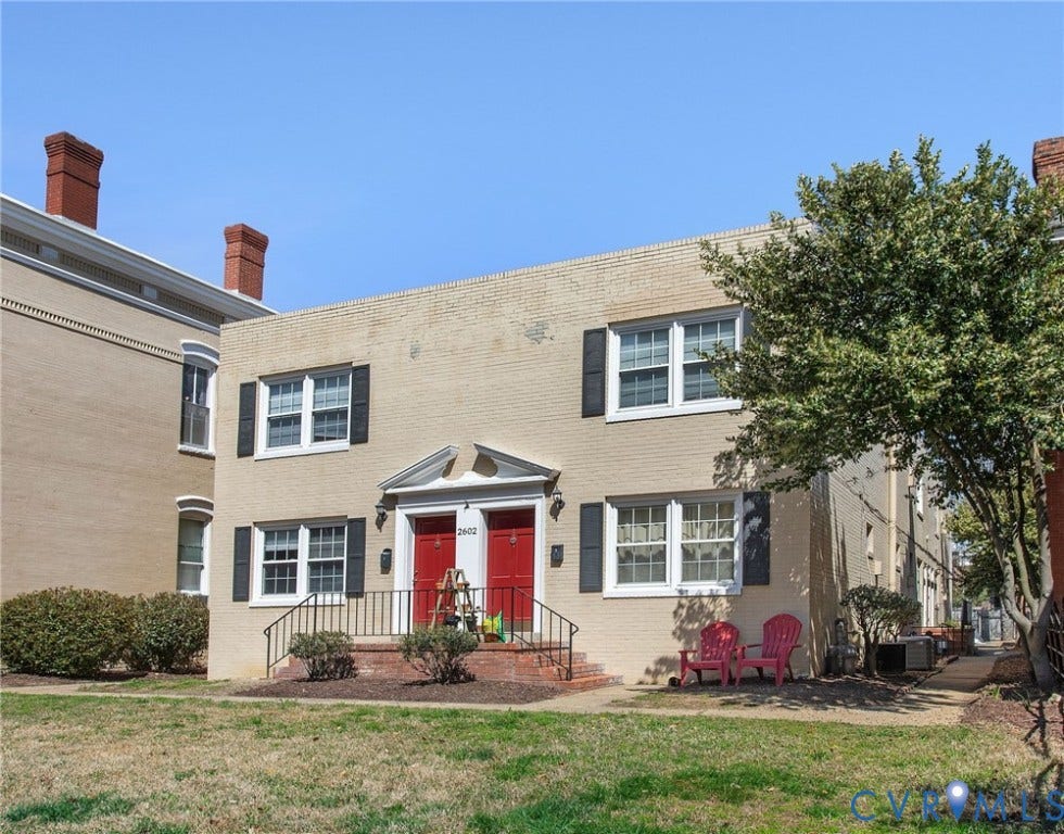 Multi-story brick exterior with dual red entry doors, white window trim, and black shutters