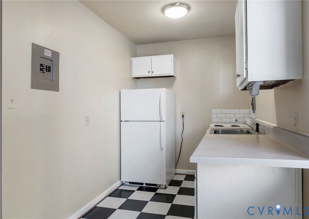 Compact kitchen featuring checkerboard flooring, white cabinetry, a single basin sink, white subway tile backsplash, and a flush-mount ceiling light