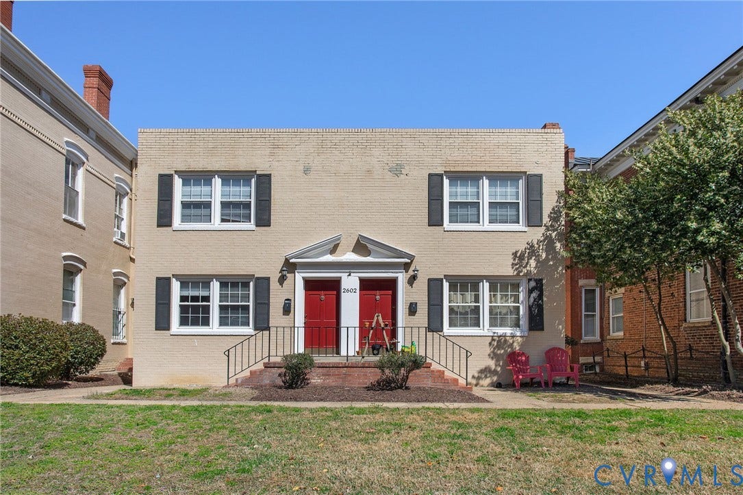 Brick facade with red entry doors, white window frames, and black shutters