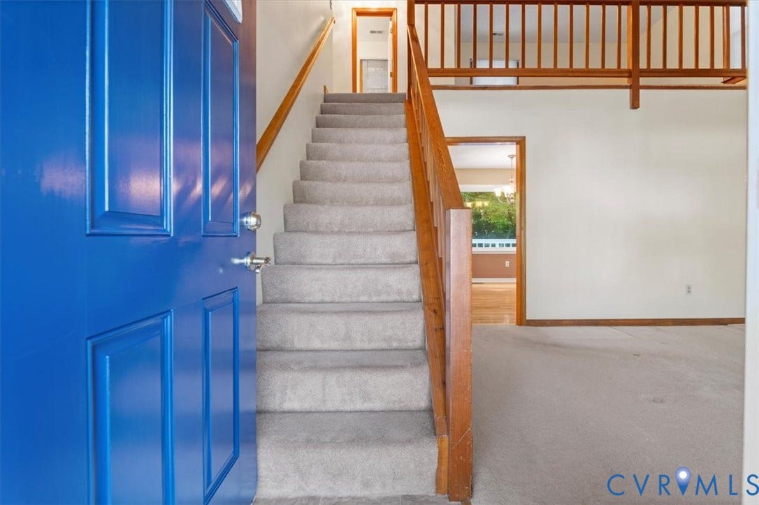 Bright blue paneled entry door, carpeted staircase with wood railing, wood-frame doorway, and wood flooring visible in background