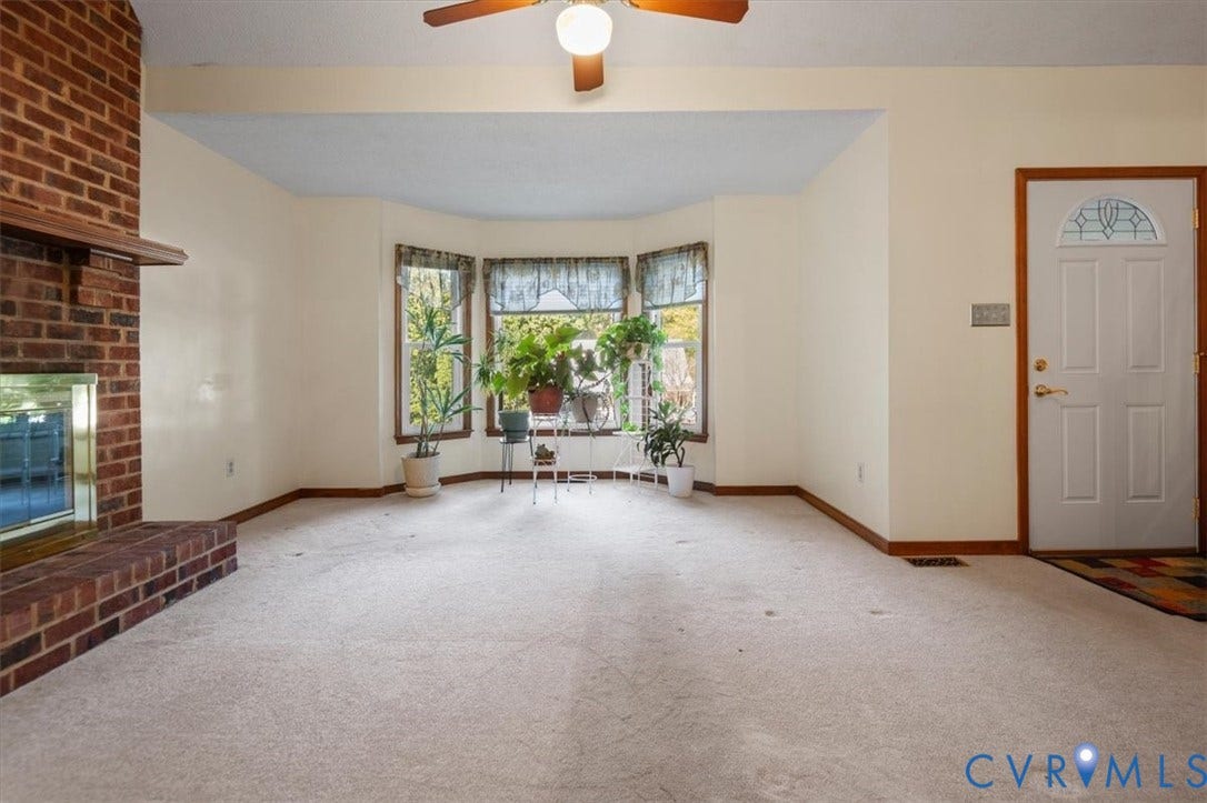 Brick fireplace with an integrated mantel, bay window, ceiling fan with integrated lighting, and a front entry door with decorative glass