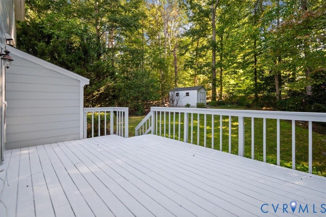 Expansive white painted deck with railing, offering views of a manicured lawn, mature trees, and a detached storage shed