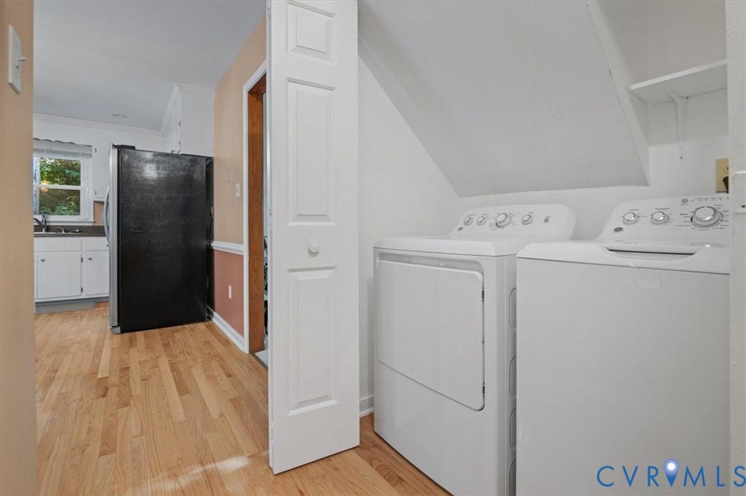 Laundry area with washer and dryer, adjacent to a kitchen featuring a black refrigerator and wood-finish flooring