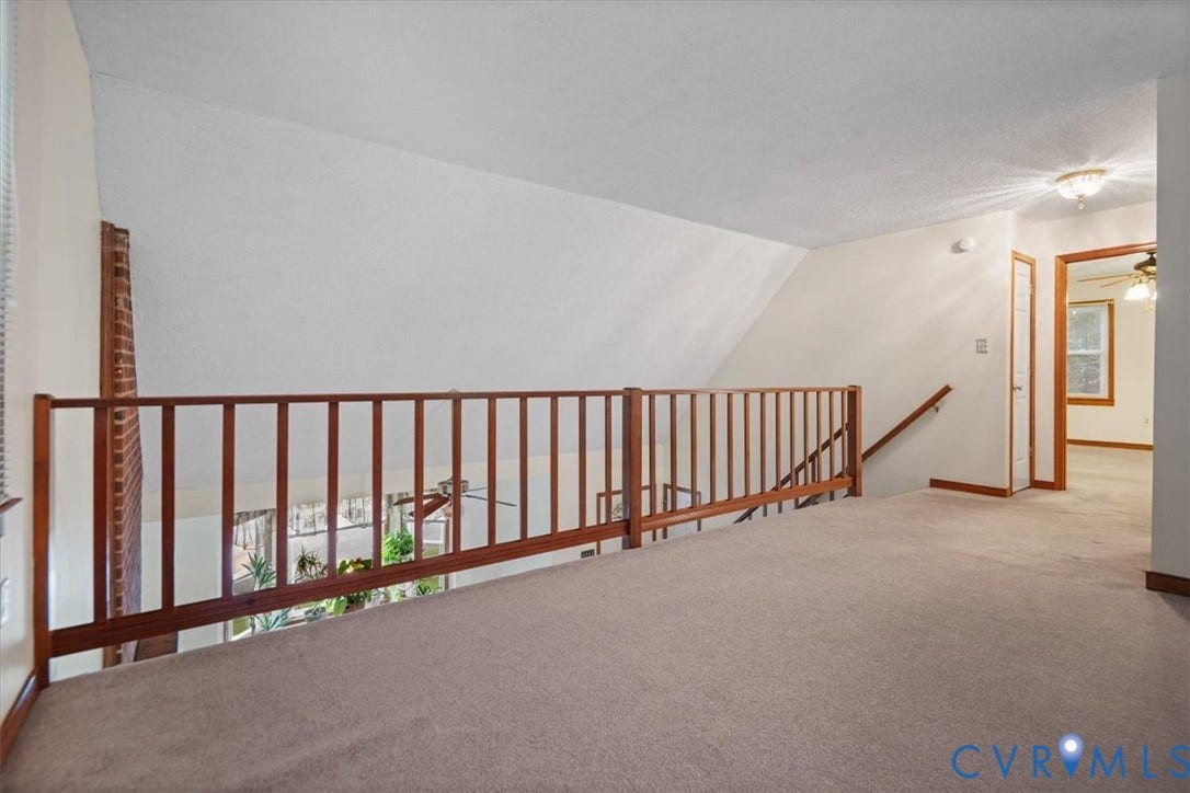 Carpeted loft space with a wooden railing and a sloped ceiling