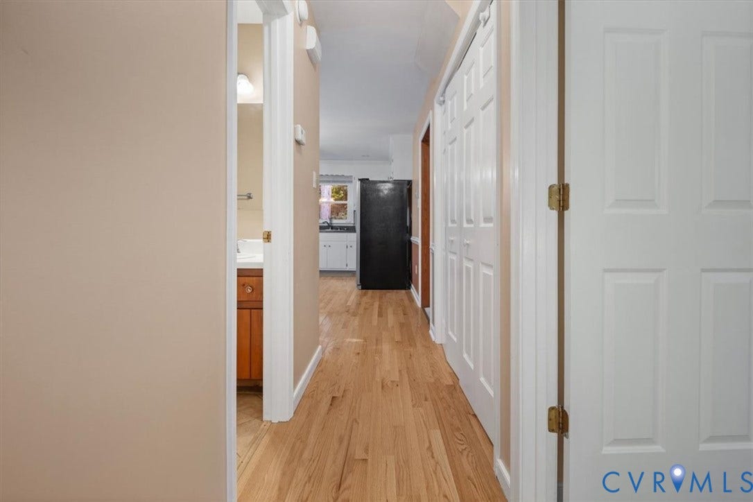 Hallway with wood-finish flooring, white panel doors, and neutral wall paint