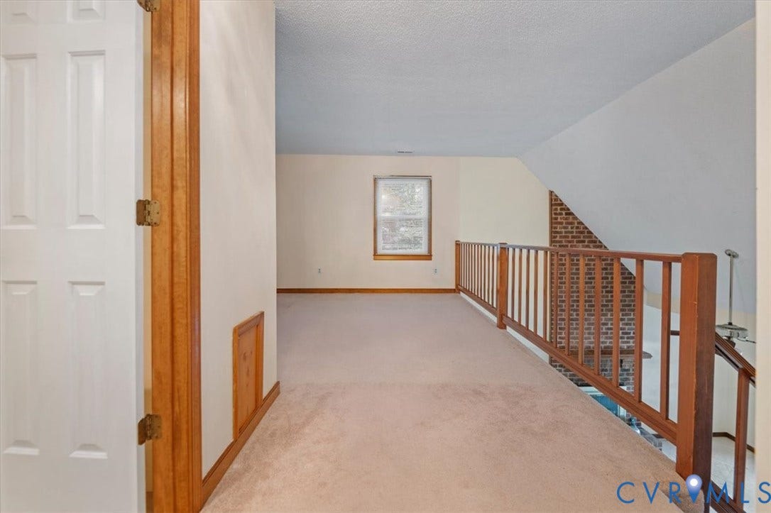 Carpeted loft area featuring a wood railing and a window with wood trim