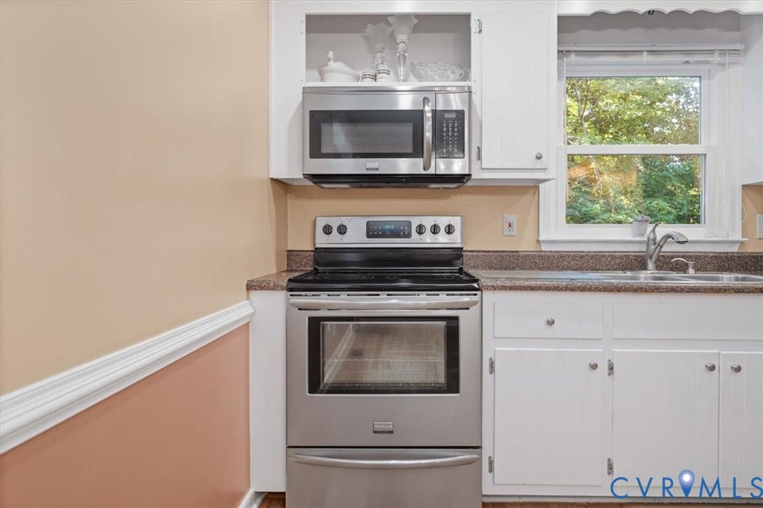 Stainless steel appliances, white cabinetry, dark speckled countertop, single basin sink, and a double-hung window
