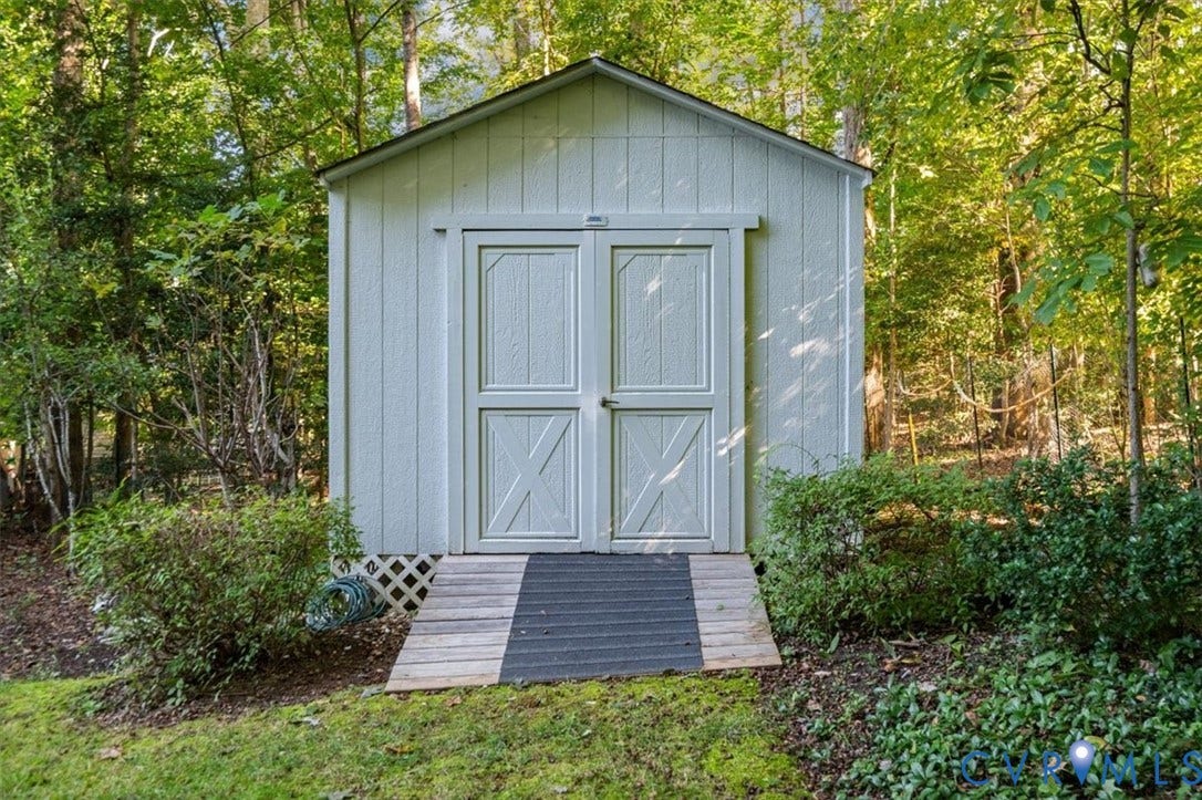 White siding shed with double barn doors, wood ramp access, and surrounding landscaping
