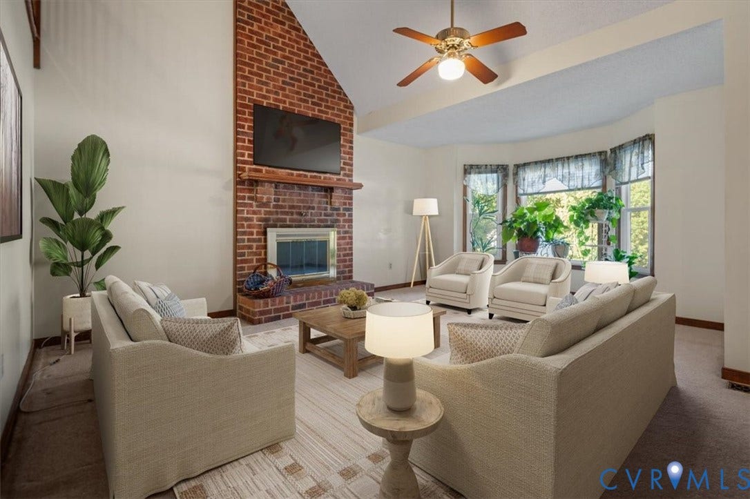 Vaulted ceiling with a ceiling fan, brick fireplace, bay window, and light-colored wall finishes