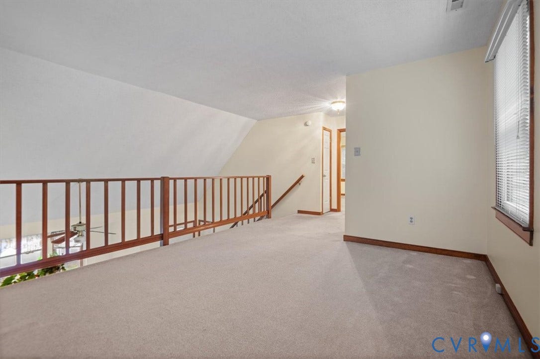 Carpeted loft area with wood railing and sloped ceiling