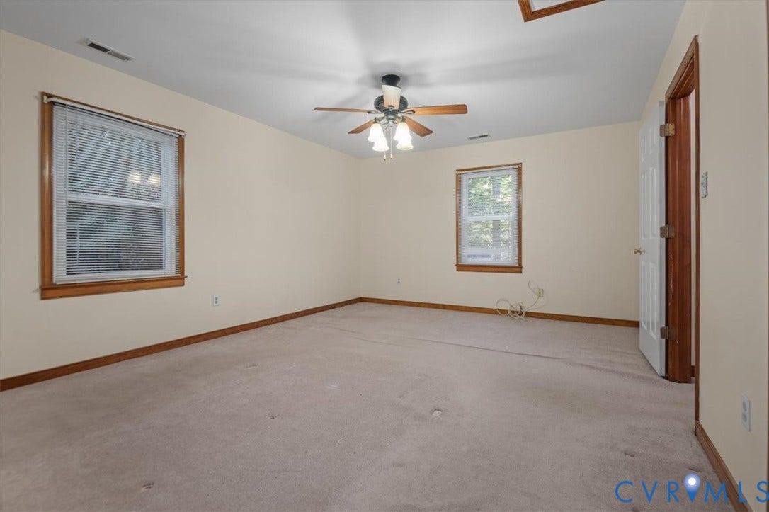 Spacious room with two windows, carpet flooring, a ceiling fan with integrated lighting, and a white paneled door
