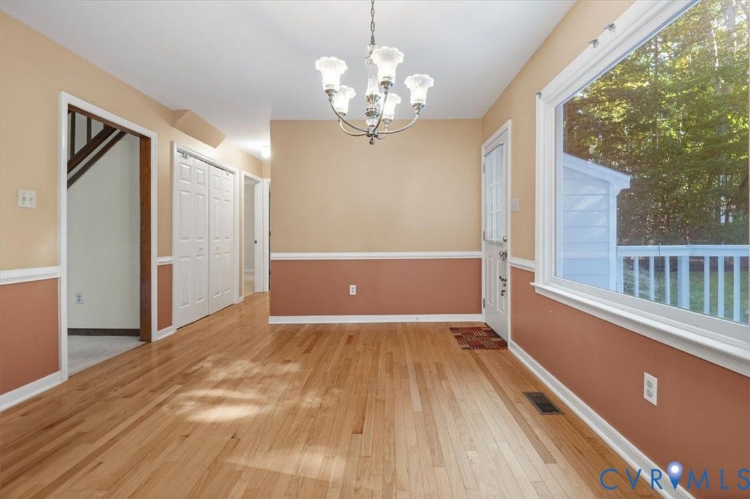 Hardwood flooring, decorative chair rail molding, a three-light chandelier, and a large window