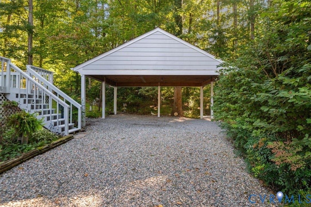 Gravel driveway leading to a covered carport, featuring white siding and a wood ceiling