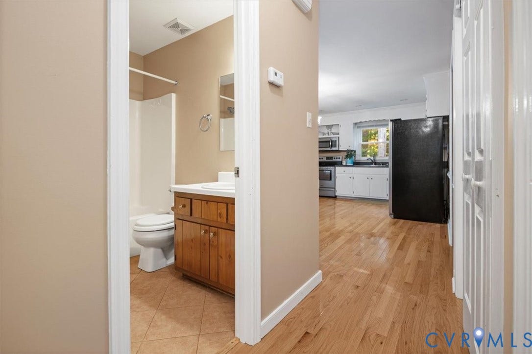 Hardwood flooring, white kitchen cabinetry, stainless steel oven, black refrigerator, and a bathroom with a wood-finish vanity