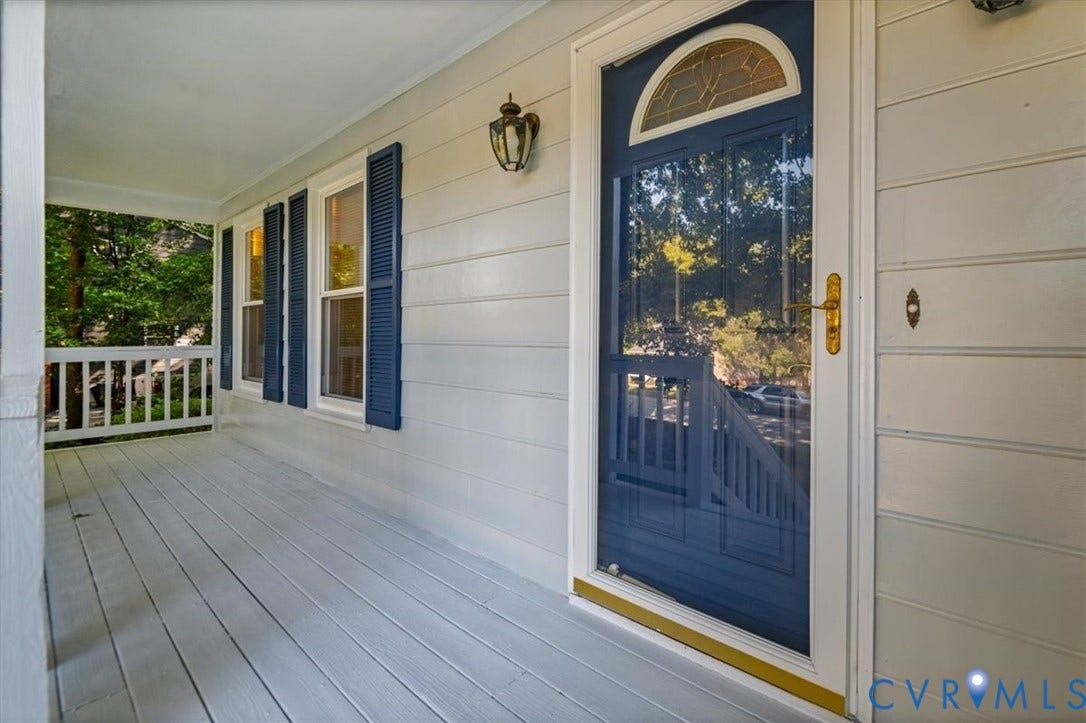 Covered front porch featuring a dark blue screen door with an arched transom, matching window shutters, and a wall-mounted light fixture