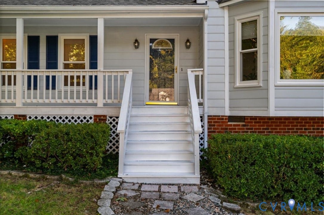 Light-colored siding exterior with a front porch, white railings, and a red brick foundation