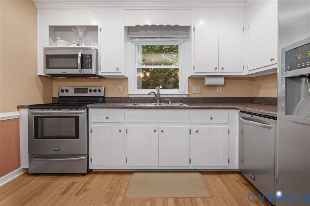 White cabinetry with contrasting hardware, stainless steel appliances, wood-finish flooring, and a window over the sink