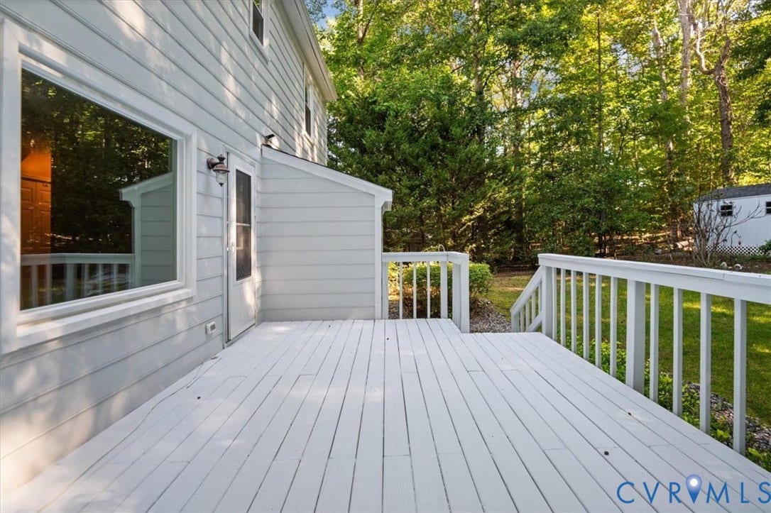 Spacious wood deck with white railing, exterior siding, and mature trees surrounding the property