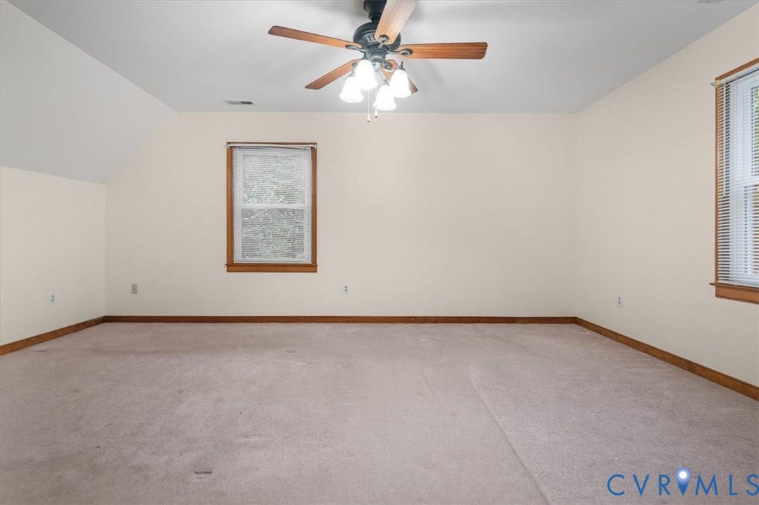 Expansive room featuring a sloped ceiling, light-toned carpeting, and a ceiling fan with integrated lighting