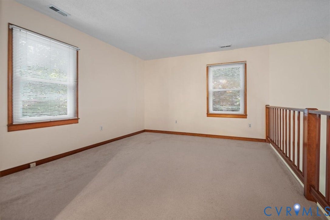 Carpeted room with two windows, a wood railing, and neutral wall paint