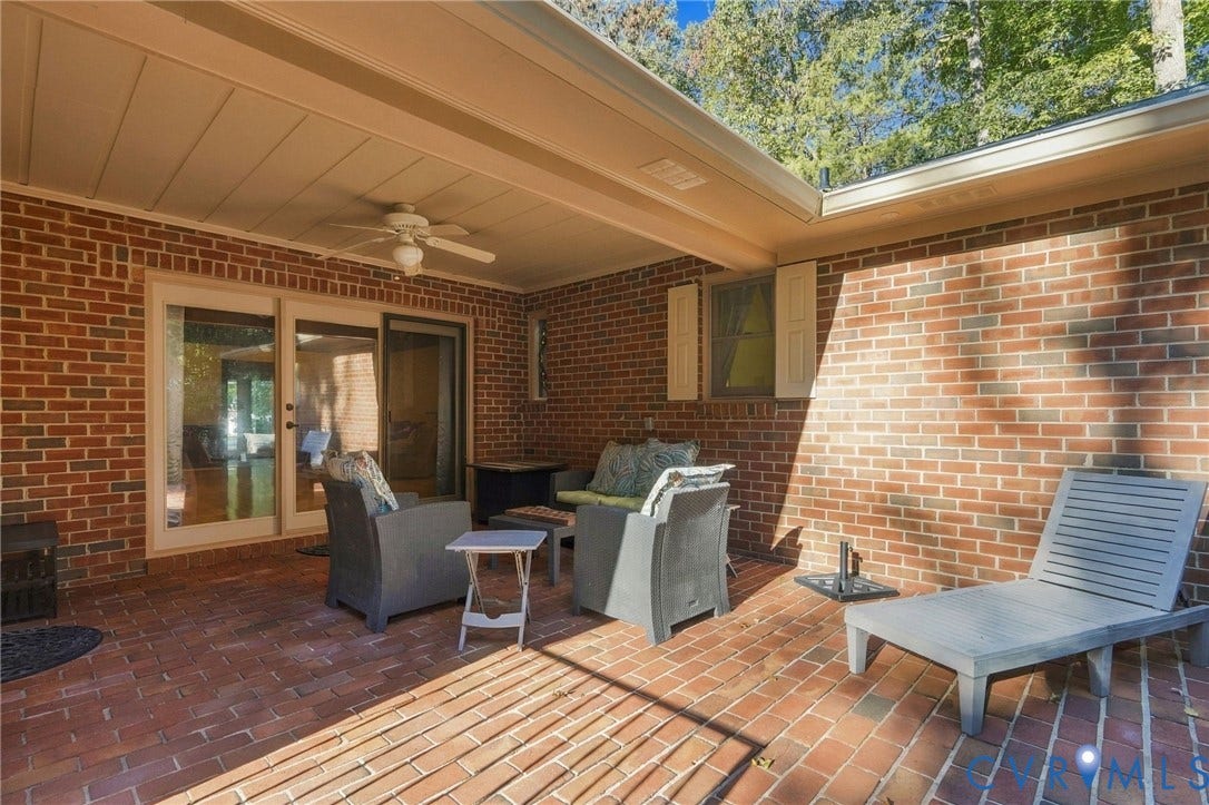Covered patio with brick flooring, brick exterior, ceiling fan, and sliding glass door
