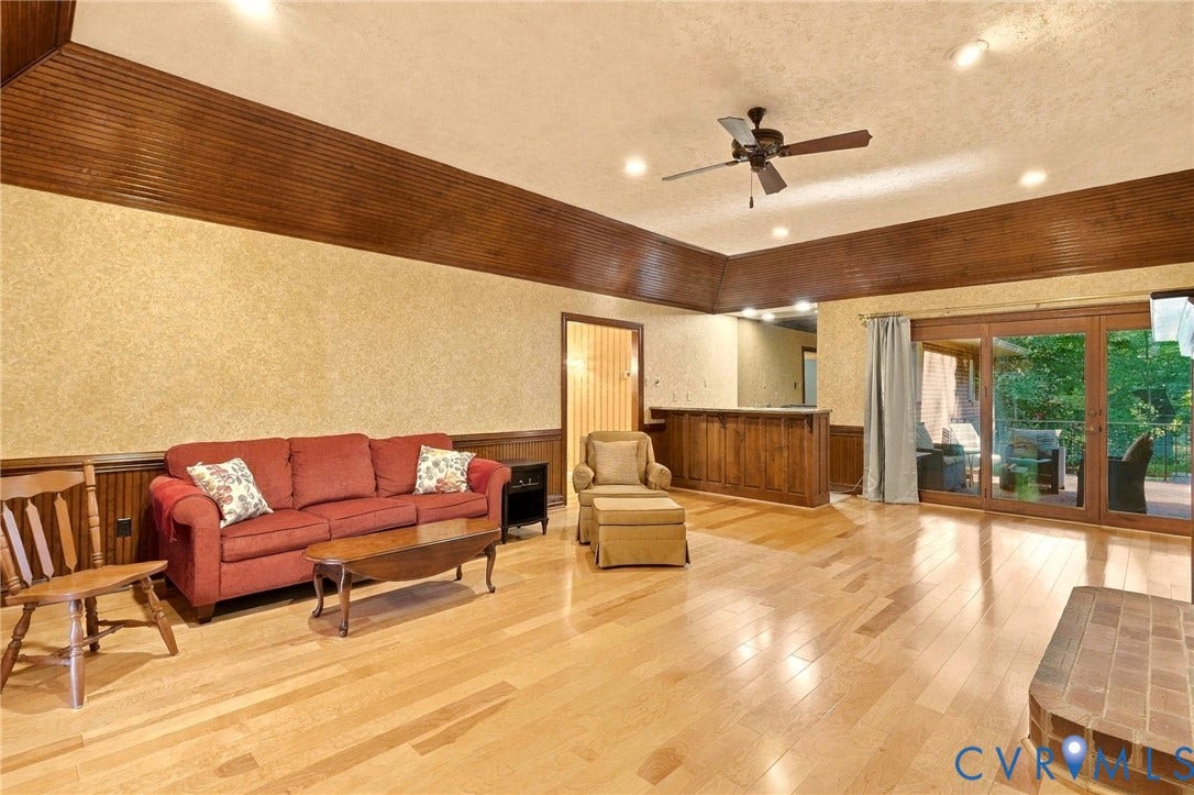 Hardwood flooring, wood-paneled accents, built-in wet bar, large glass patio doors, and a brick fireplace