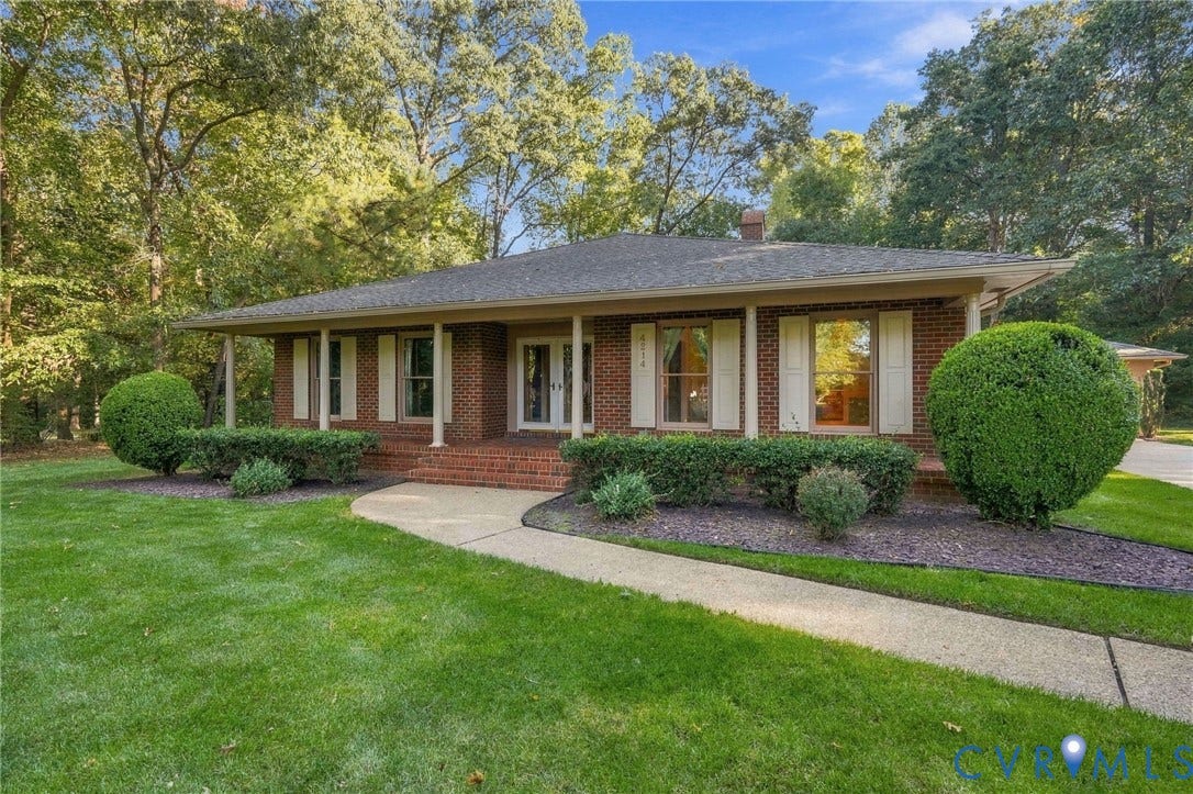 Brick exterior with a covered front porch supported by columns, a concrete pathway, a shingled roof, and mature landscaping