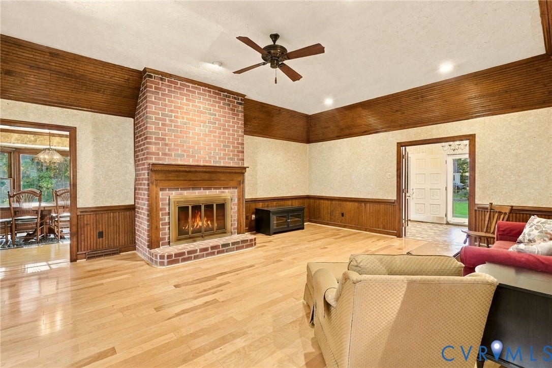 Hardwood flooring, brick fireplace with wood mantel, wood paneling, wood-finish ceiling fan, and recessed lighting