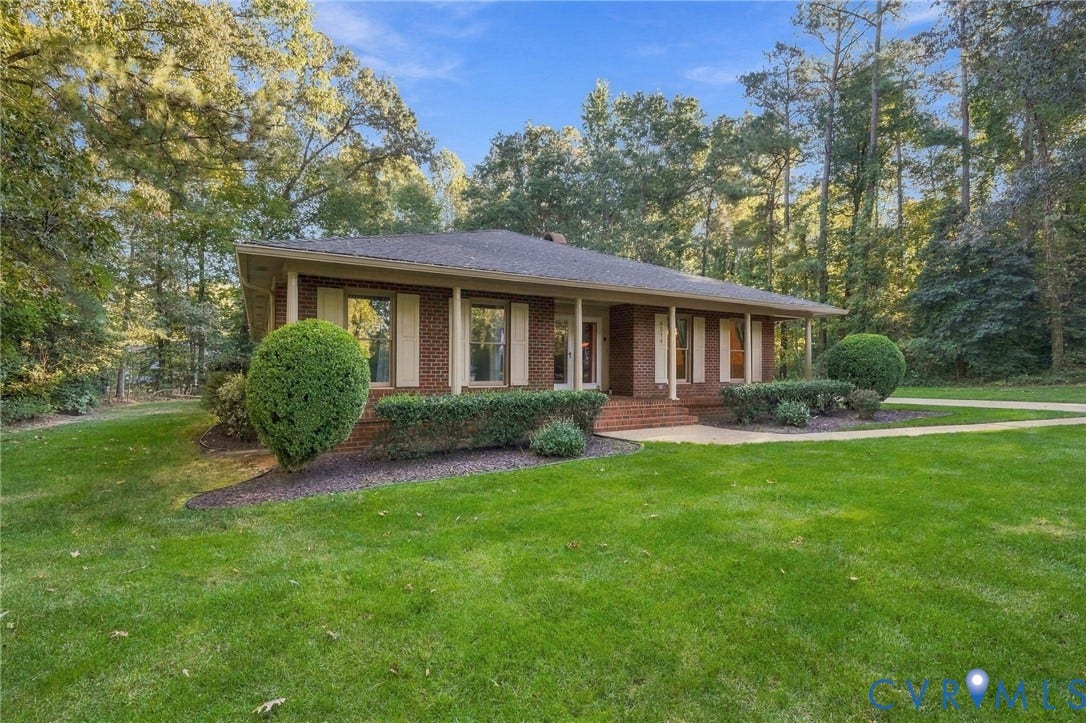 Brick-clad residence featuring a covered front porch and mature landscaping