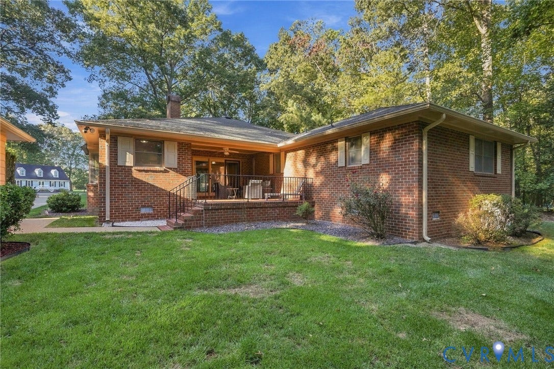 Brick exterior featuring an expansive covered patio with a ceiling fan, a front lawn, and mature trees